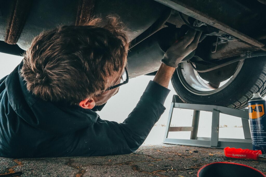 pexels-photo-2244746-2244746 Mechanic skillfully repairing car undercarriage in outdoor setting with tools.
